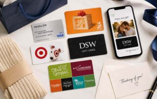Flat lay of a thoughtfully arranged collection of physical and digital gift cards, a smartphone displaying a personalized digital gift card, stationery, ribbon, and gift packaging, representing creative and flexible ways to give gift cards.